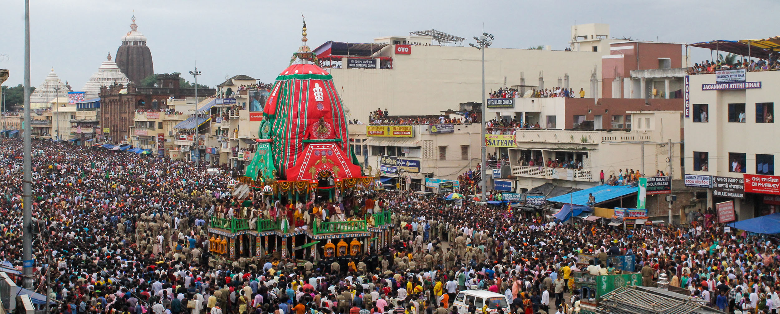 Aerial view of a large crowd participating in the vibrant Rath Yatra festival procession with a decorated chariot on the street. Aerial view of a large crowd participating in the vibrant Rath Yatra festival procession with a decorated chariot on the street.